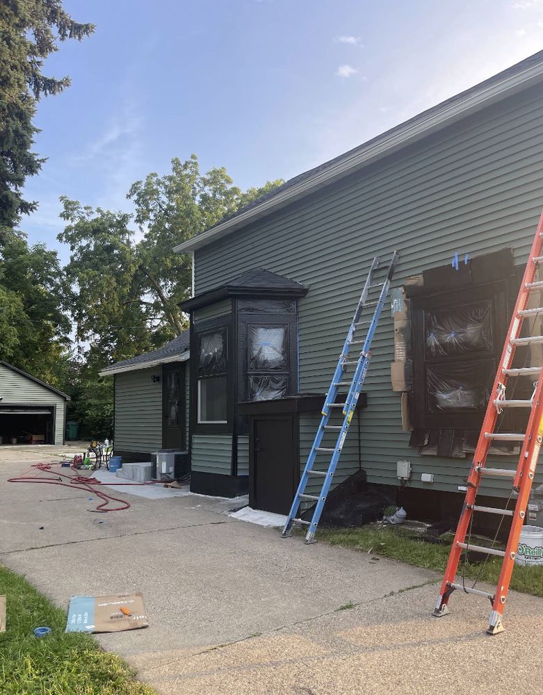 Exterior repaint in progress, with windows masked off and ladders set against green siding